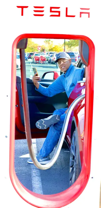A man seated in a red car, framed in a charging-station mirror