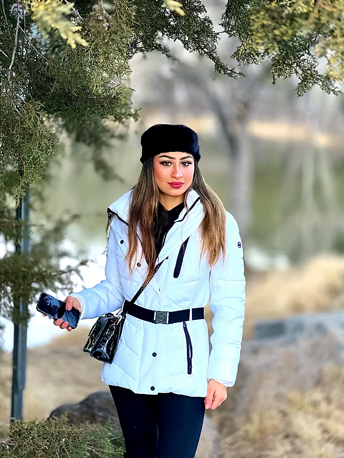 A woman in a white winter jacket and black fur headband beside a lake