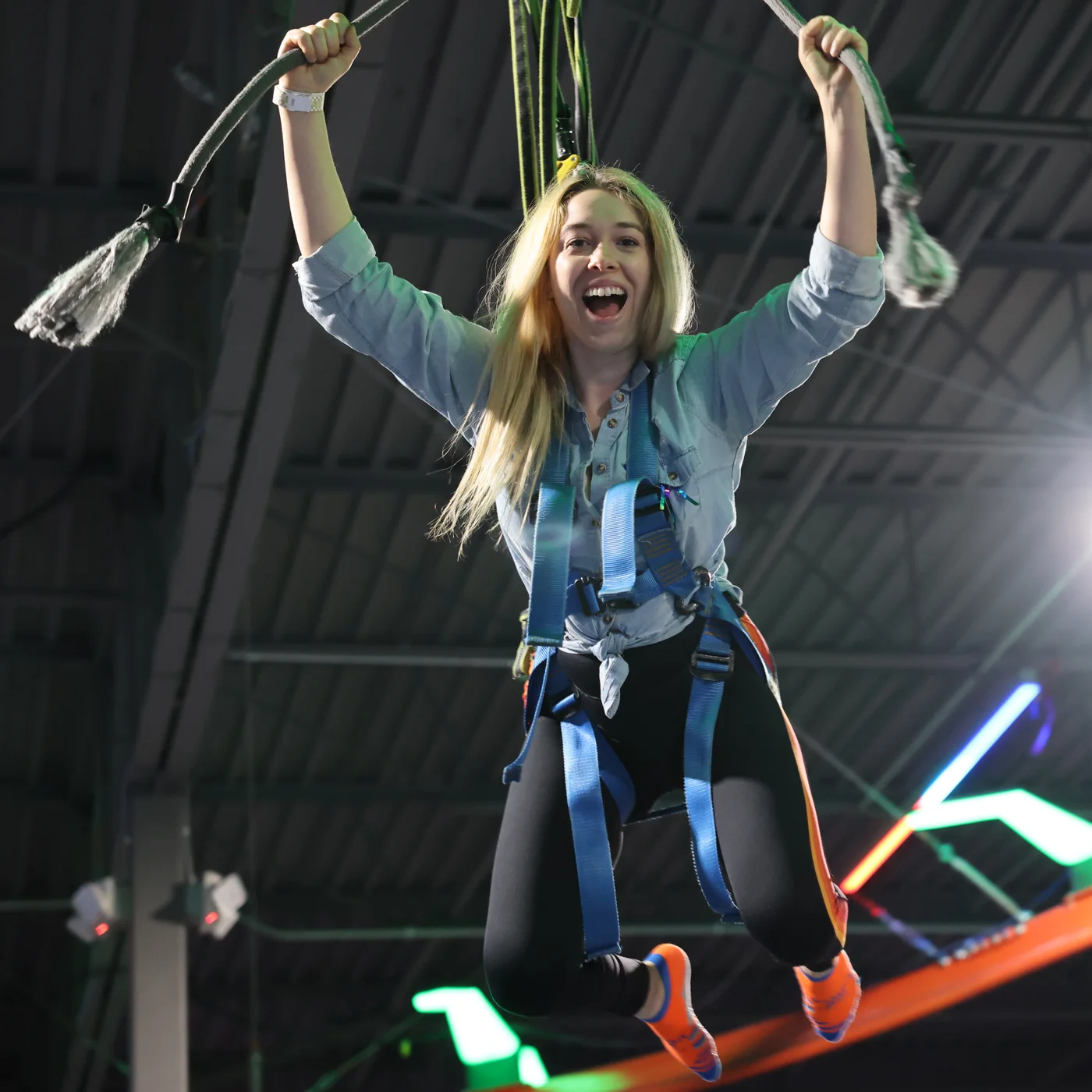 A woman grinning with both arms raised on an indoor sky-rope ride